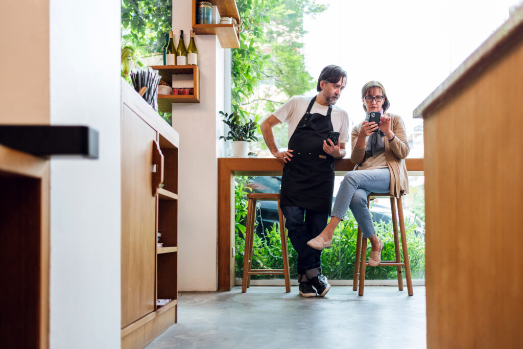 Cafe owner consults with financial advisor using smartphone, seated in modern coffee shop. Scene captures teamwork, planning, and smart collaboration in small business management and strategy.