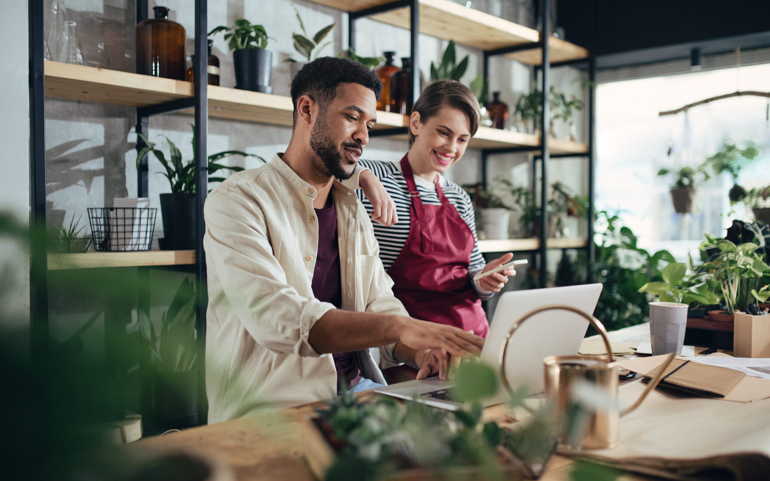 Shop assistants with laptop working in potted plant store, small business concept.